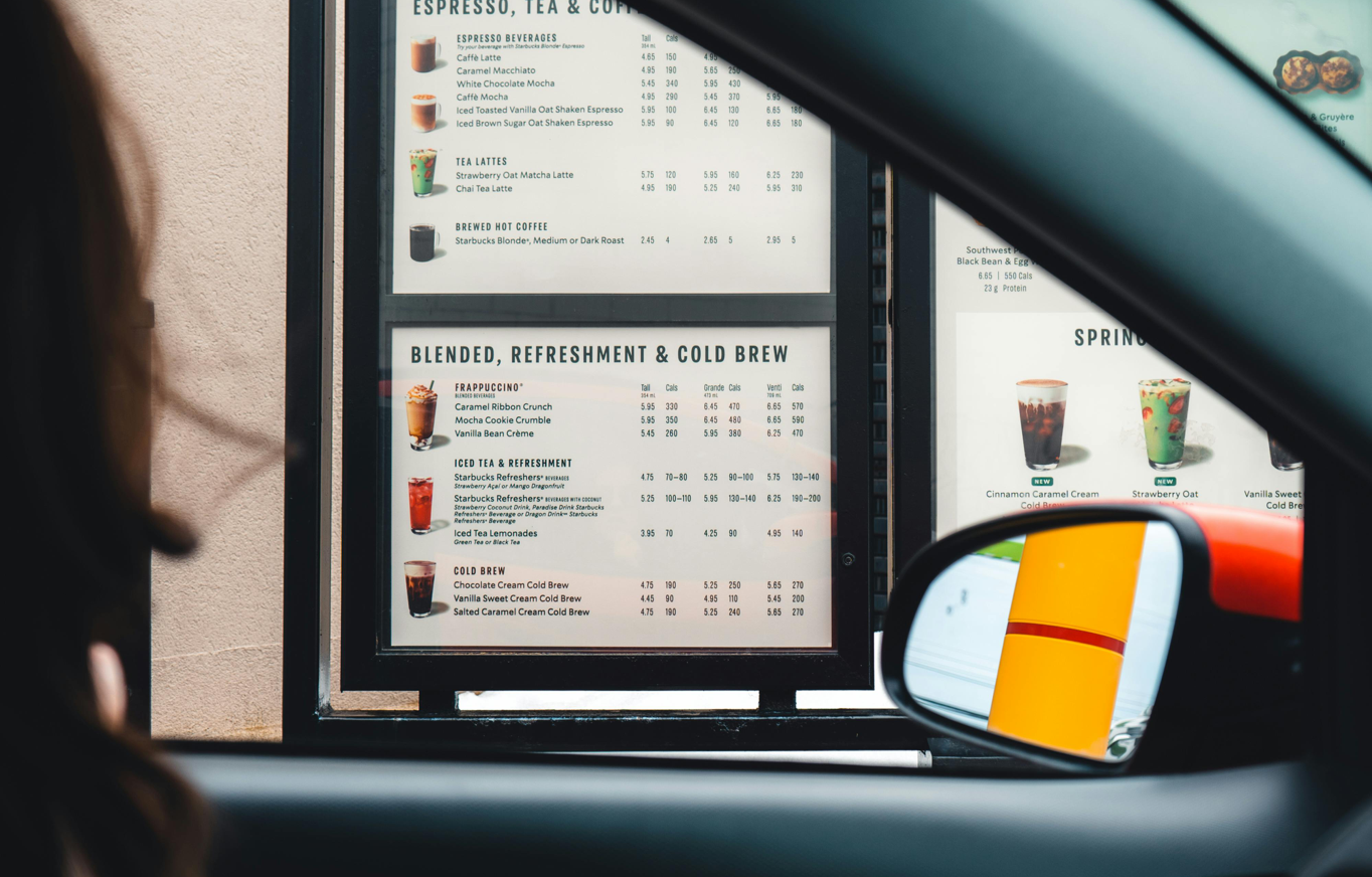 View of a coffee shop menu from a car window at a drive-thru, showcasing beverage options.