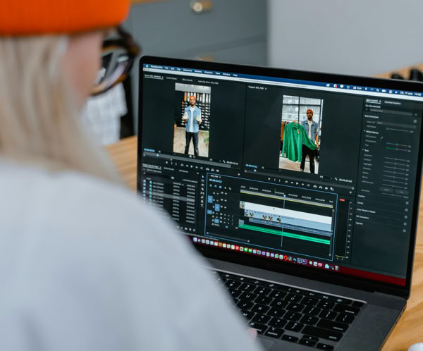 Woman focused on video editing using a laptop in a modern office setting with a bright orange hat.