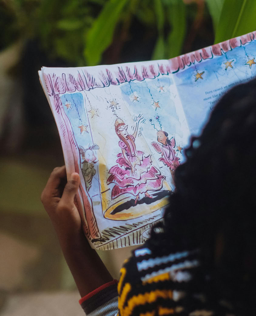 A child reads an illustrated storybook outdoors, captivated by colorful fairy-tale images.